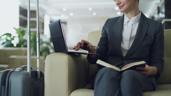 Tilt Up of Blonde Businesswoman Sitting in Armchair in Hotel Lobby Writing in Notepad and Using alt