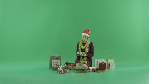 A Young Woman Is Sitting and Opening Christmas Gift Near Herself on the Green Screen