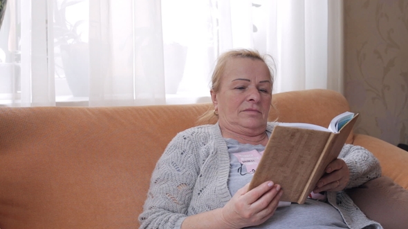 Senior Woman Sitting on Sofa and Reading a Book