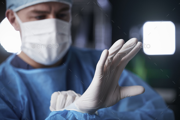 Male surgeon putting on latex gloves in preparation Stock Photo by monkeybusiness