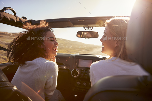 Two girlfriends driving with sunroof open look at each other Stock Photo by monkeybusiness