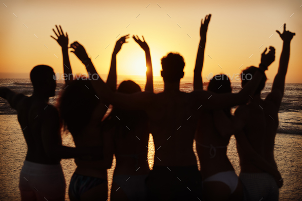 Silhouette Of Friends On Beach Vacation Watching Sunset Over Sea Stock  Photo by monkeybusiness