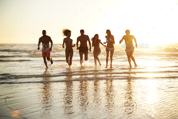 Group Of Friends Run Through Waves Together On Beach Vacation Group Of Friends Run Through Waves Together On Beach Vacation
