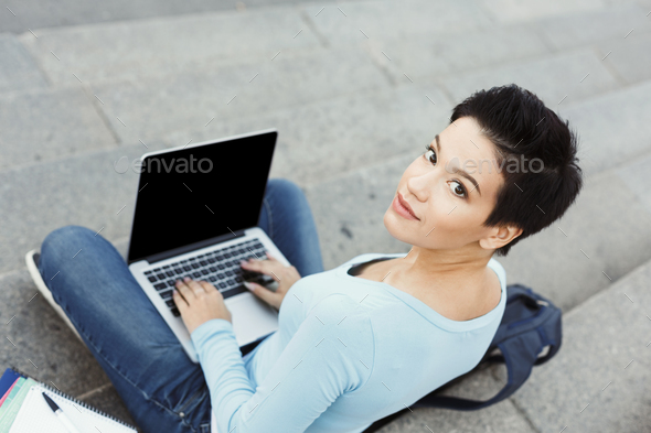 Smiling young woman using laptop outdoors - Stock Photo - Images