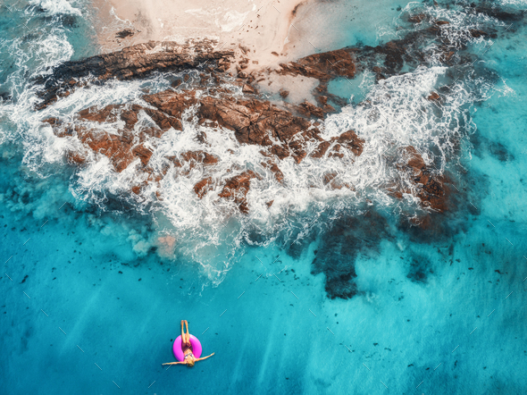 Aerial view of young woman swimming on the pink swim ring in the transparent turquoise sea - Stock Photo - Images