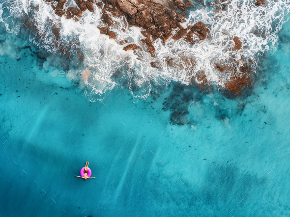 Aerial view of young woman swimming on the pink swim ring in the transparent turquoise sea - Stock Photo - Images