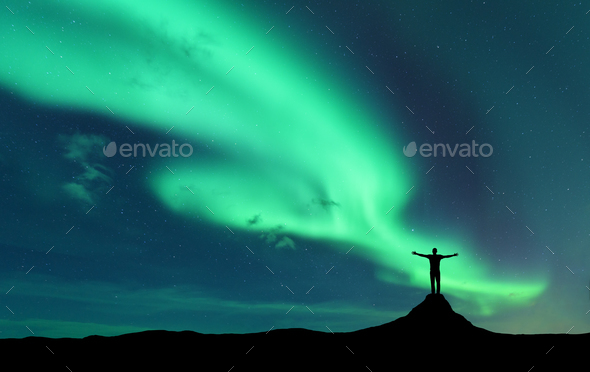 Aurora and silhouette of standing man with raised up arms on the mountain in Norway - Stock Photo - Images