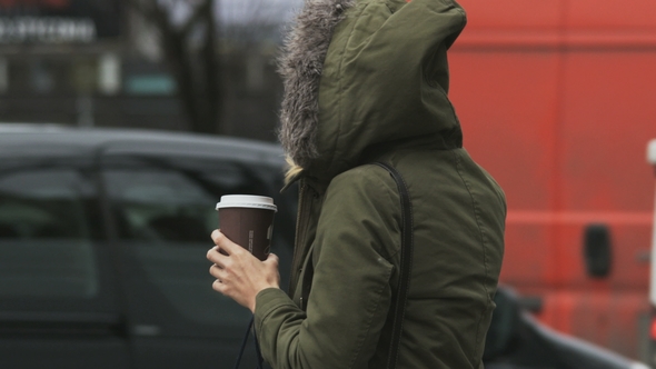 Hooded Young Woman in Green Jacket Holding a Coffee Bin