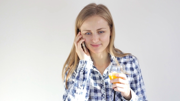 Young Woman with a Glass of Juice Talks on Mobile Phone