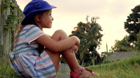 Happy Little Girl Sitting on the Grass and Playing in Summer Garden. Outdoors