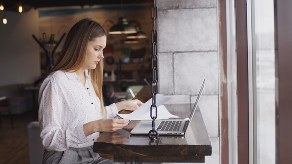 Beautiful Businesswoman in a White Shirt Working at a Laptop in a Cafe