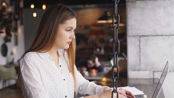 Beautiful Businesswoman in a White Shirt Working at a Laptop in a Cafe
