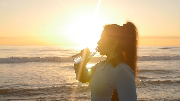 Young Sporty Woman Drinking Water Outdoor on Sunset Near Sea