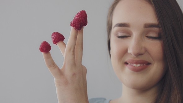 Young Caucasian Woman with Straight Long Hair Eats Raspberry From Fingers