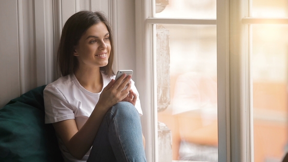 Joyful Woman Uses Gadget Near Window