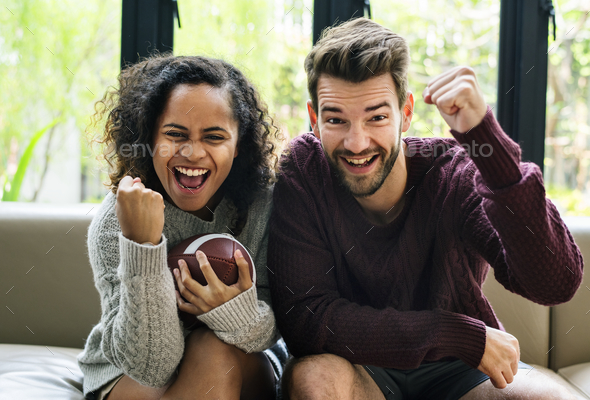 Young couple watching american football at home Stock Photo by Rawpixel
