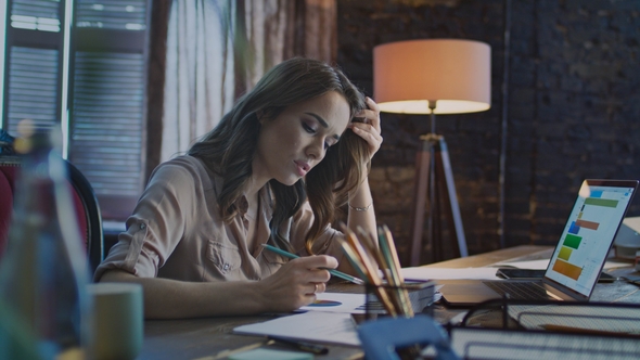 Concentrated Businesswoman Making Notes at Table with Laptop in Office alt