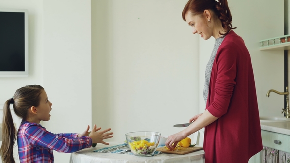 Cute Daughter and Cheerful Mother Talking in Modern Kitchen During Cooking. Mom Feeding Her Girl alt