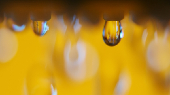 Shining Drops of Water Running From a Metallic Nozzle in a Yellow Bathroom