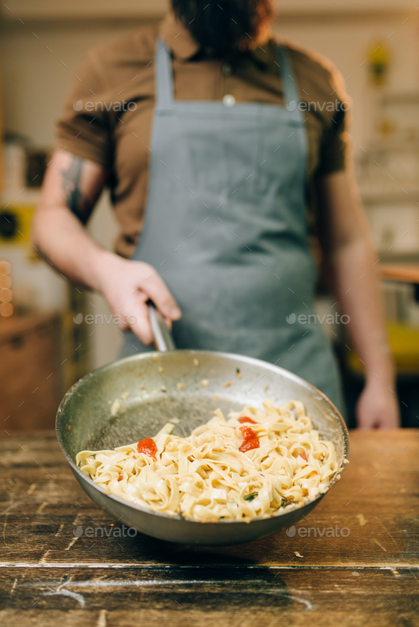 Male chef holds pan with pasta, fettuccine cooking - Stock Photo - Images