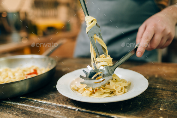Male chef puts fresh pasta in a plate - Stock Photo - Images