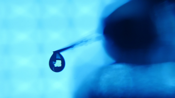 Clean Drops of Water Fall From a Syringe Needle in a Blue Medical Laboratory
