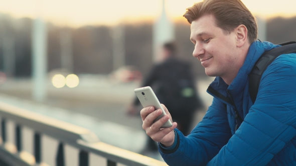 A Young Man Uses a Mobile Phone at Sunset in the City