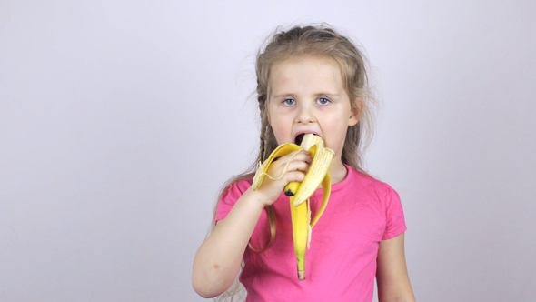 A Young Girl Bites a Banana and Shows Her Thumb Up