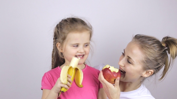 Young Mother with Her Daughter Smiling and Eating Banana and Apple