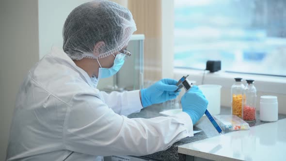 Man Employee Measures Pills and Writes Report at Table in Pharmaceutical Company Spbas alt