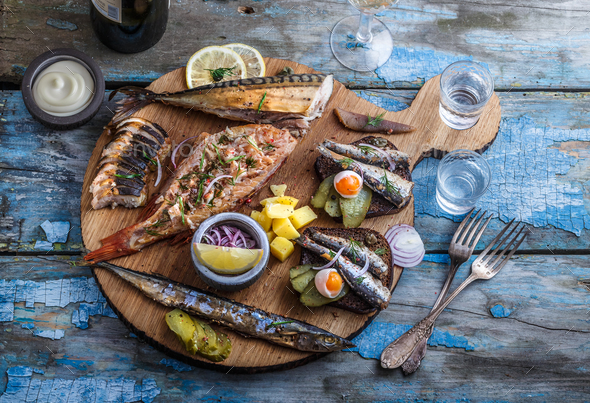 Smoked fish appetizers with mackerel, sturgeon, perch on woden cutting board Stock Photo by fazeful