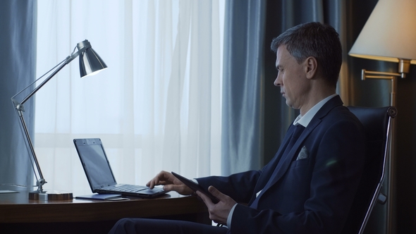 Adult Businessman Using Phone and Laptop alt