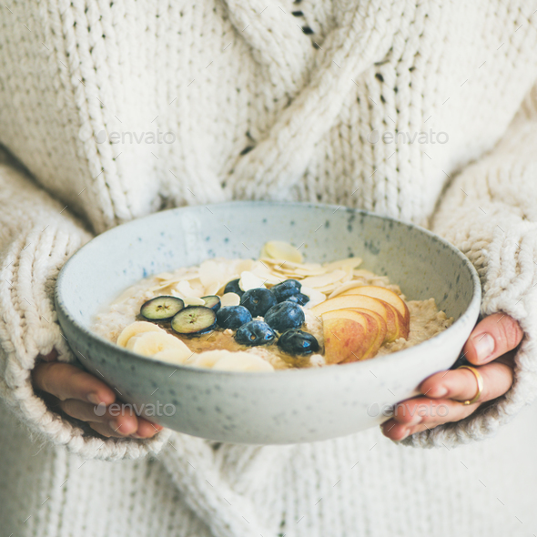 Woman in sweater holding bowl of oatmeal porriage, square crop - Stock Photo - Images