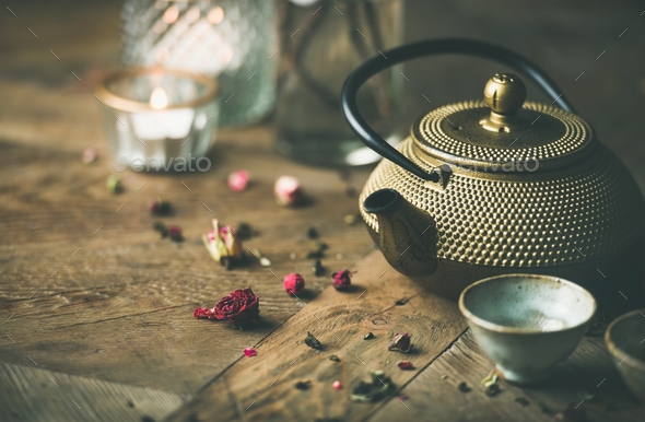 Golden iron teapot, cups, dried rose, candles over wooden background - Stock Photo - Images