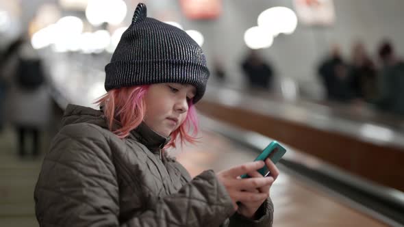 A Young Beautiful Teenage Girl is Climbing Into the Subway Using a Smartphone with the Internet to alt