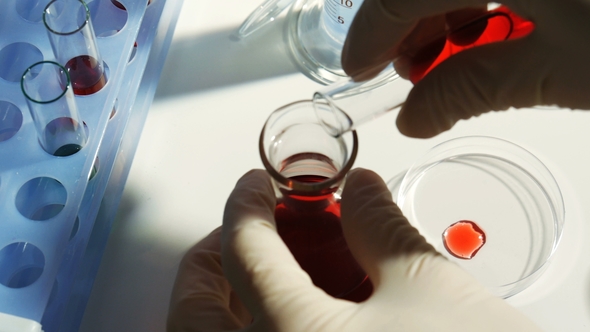 Lab Worker Pours Chemicals From a Test Tube Into a Flask