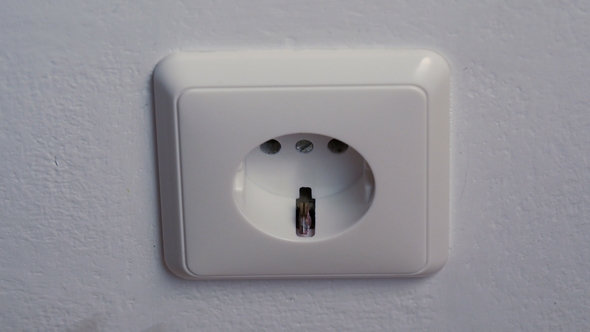 Hand Puts a Power Plug in the Wall Socket