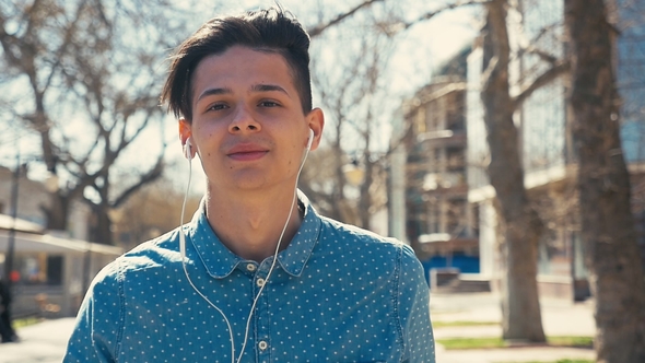 Stylish Man Goes in a Park with Earbuds in Ears in Spring in