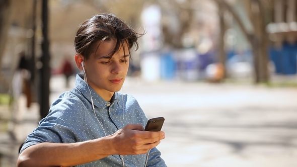 Young Man Sits on a Bench and Listens To the Music From a Mobile in Spring
