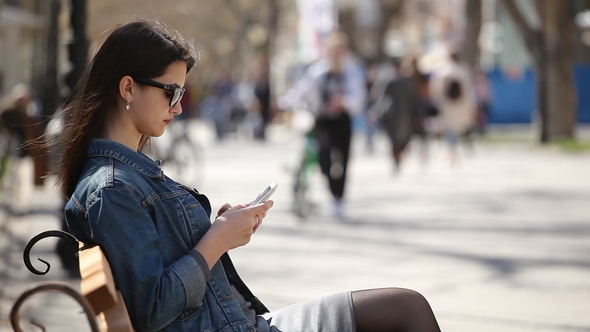 Successful Woman Surfing the Net on Her Smartphone Sitting on an Alley Bench