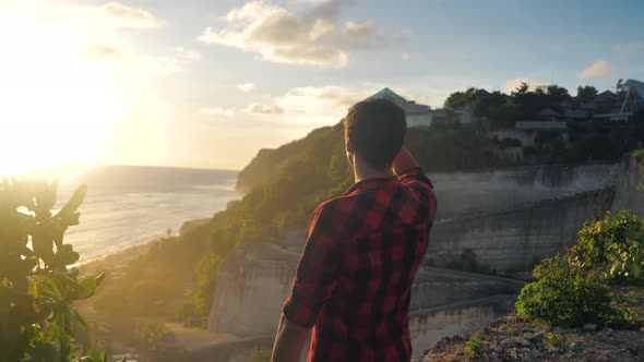 Young Male Traveler Enjoying Beautiful Sunset While Standing on a Rock on a Background of the Sea