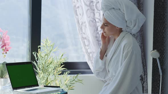 Attractive young brunette Woman in bathrobe applying foundation with beauty blender alt