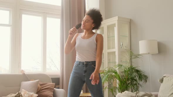 Happy african american black woman dancing jumping at home. Singing karaoke on the hairbrush alt