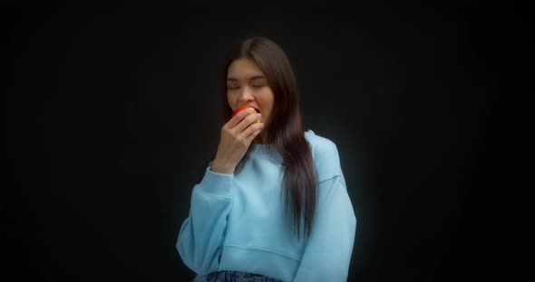 Young Beautiful Brunette in a Blue Jumper Bites a Red Apple