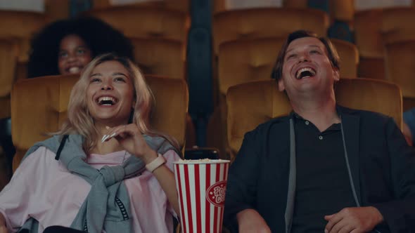 Attractive cheerful young caucasian couple laughing while watching film in movie theater.