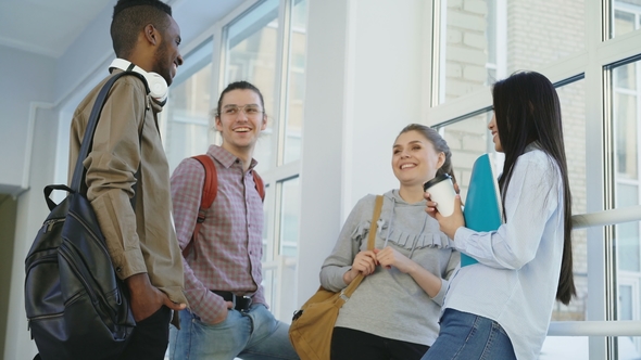 Multi-ethnic Group of Students Is Standing in Wide Corridor Near Window in College Communicating alt