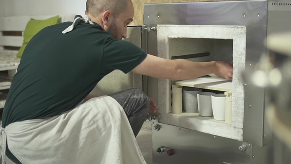 In the Pottery Workshop Man Puts Clay Pots for Firing in the Oven. alt