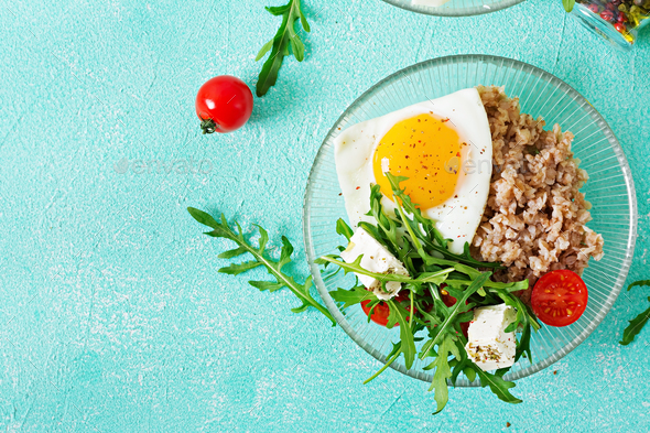 Healthy breakfast with egg, feta cheese, arugula, tomatoes and buckwheat porridge - Stock Photo - Images