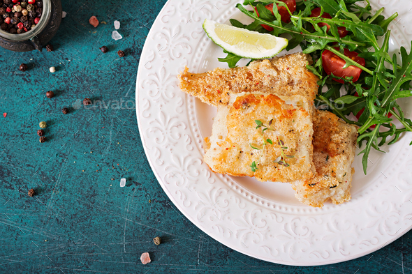 Fried white fish fillets and tomato salad with arugula. Top view Stock Photo by Timolina