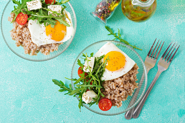 Healthy breakfast with egg, feta cheese, arugula, tomatoes and buckwheat porridge Stock Photo by Timolina